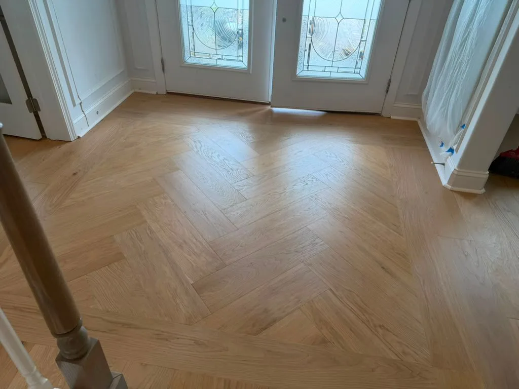 Herringbone hardwood floor at a front entry beside a stair newel