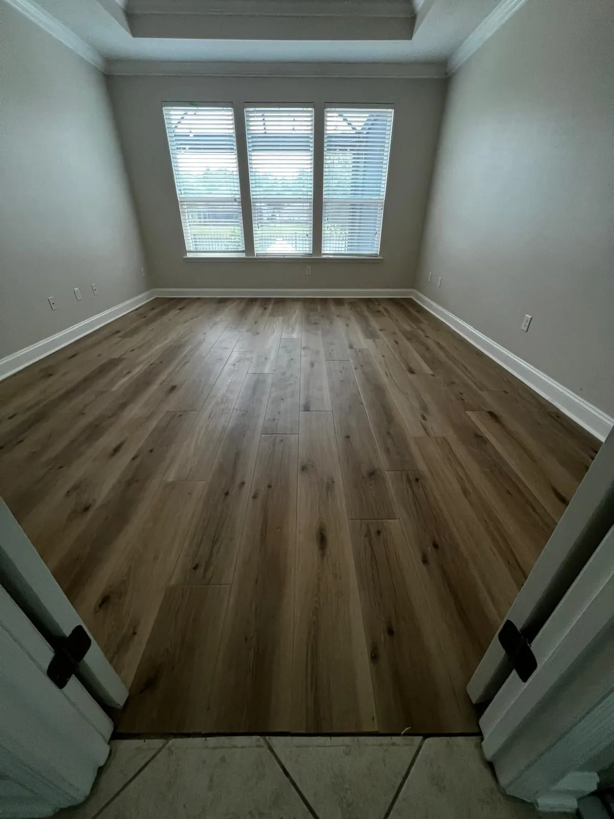 Luxury vinyl plank flooring in a bedroom with a shuttered window