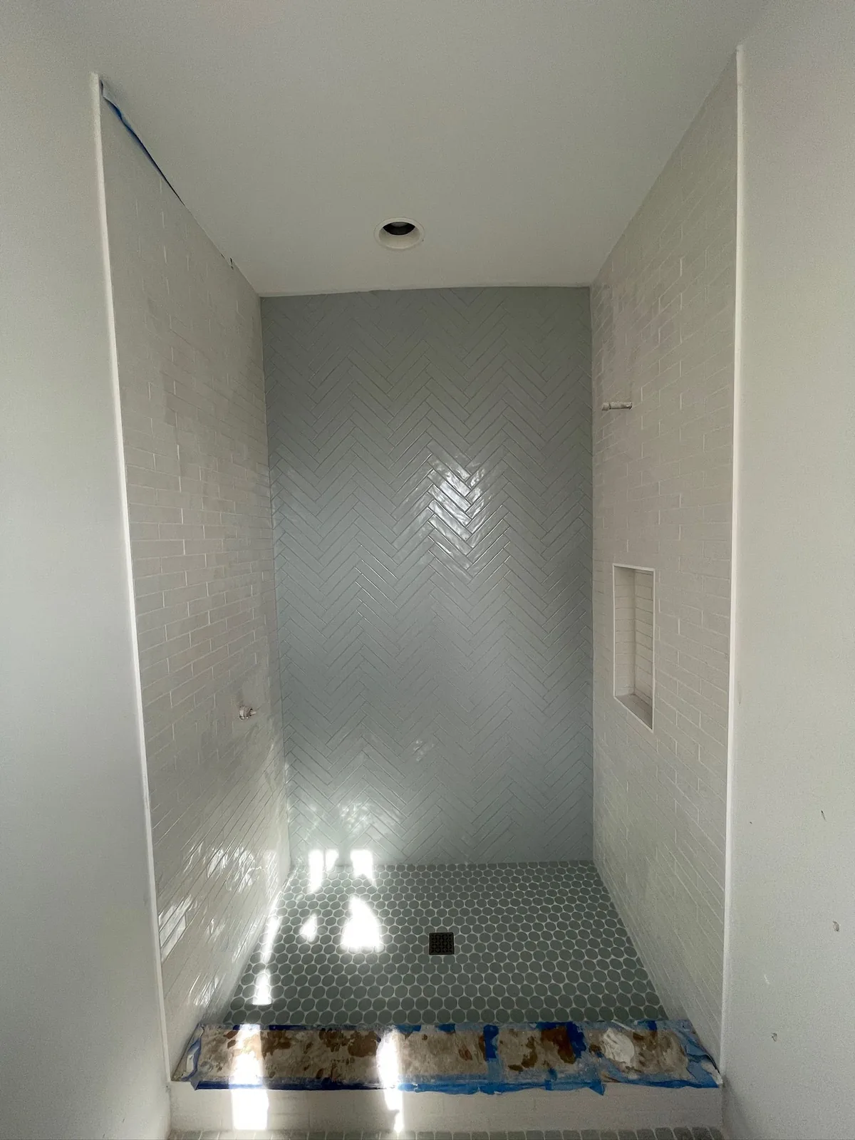 Shower with a herringbone tile back wall and hex tile floor